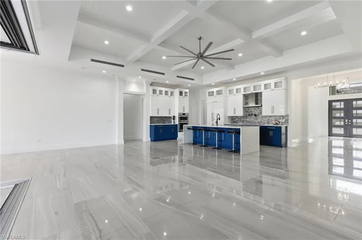 Unfurnished living room with coffered ceiling, recessed lighting, beam ceiling, french doors, and bar with sink