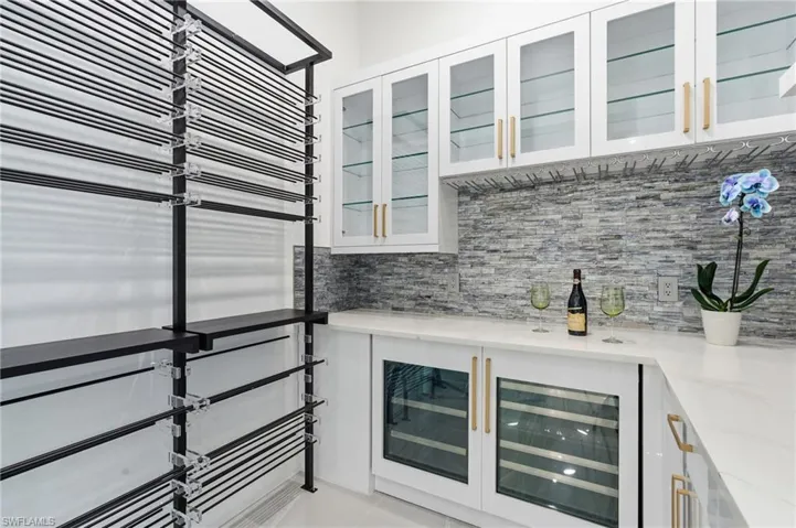 Bar area with glass insert cabinets, beverage cooler, light stone countertops, and white cabinetry