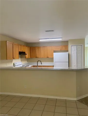 Kitchen with under cabinet range hood, light countertops, white appliances, and visible vents