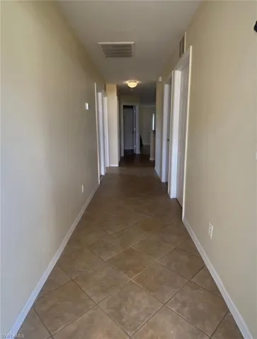 Hallway with tile patterned flooring, visible vents, and baseboards