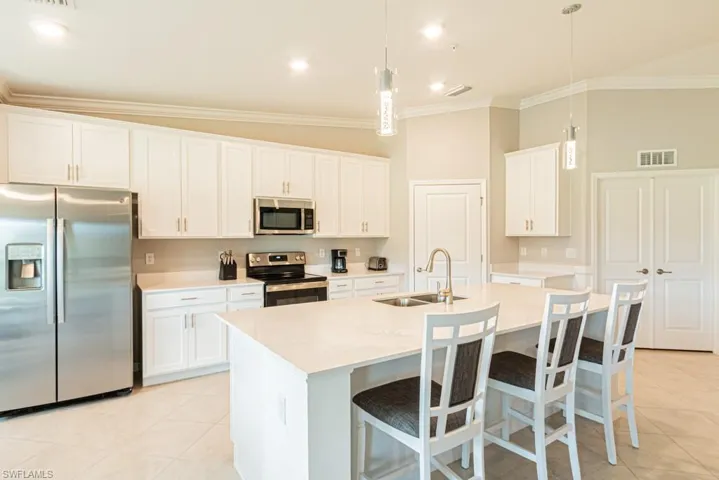 Kitchen featuring appliances with stainless steel finishes, ornamental molding, light tile patterned flooring, light countertops, and a kitchen bar