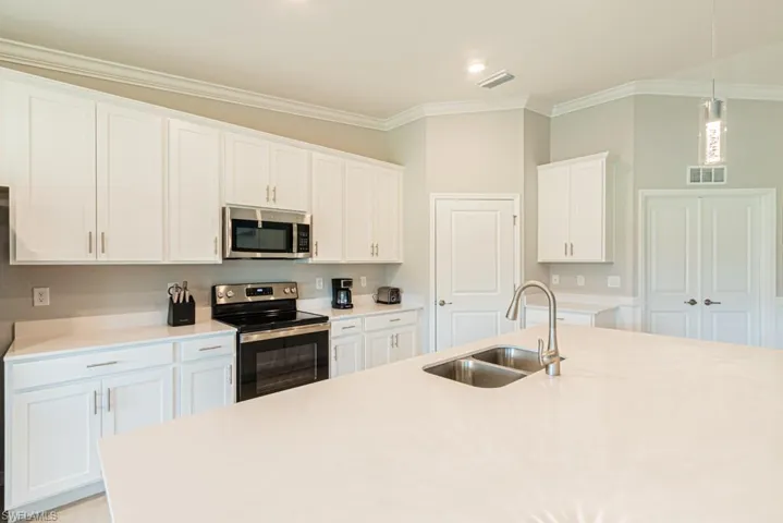 Kitchen with appliances with stainless steel finishes, ornamental molding, light countertops, white cabinetry, and decorative light fixtures