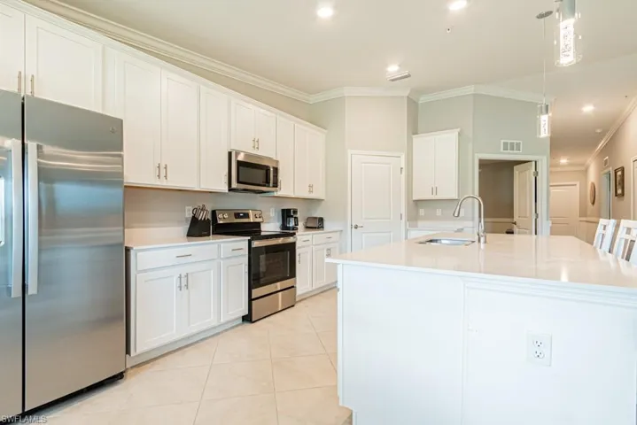 Kitchen featuring appliances with stainless steel finishes, ornamental molding, white cabinets, light tile patterned flooring, and a kitchen island with sink