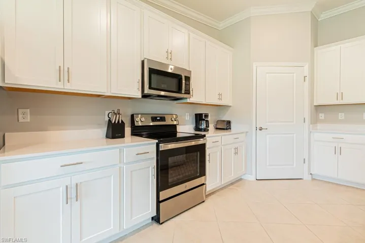 Kitchen with stainless steel appliances, crown molding, light countertops, white cabinets, and light tile patterned floors