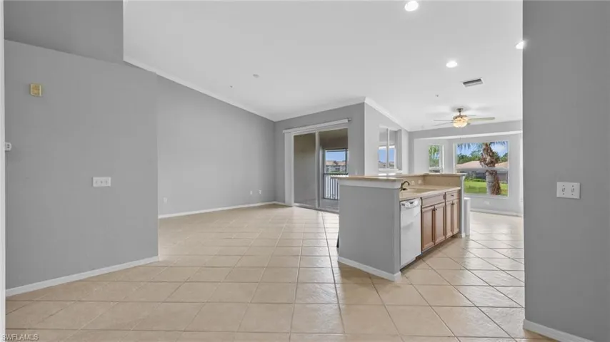 Kitchen featuring light countertops, light tile patterned flooring, ornamental molding, recessed lighting, and a center island with sink