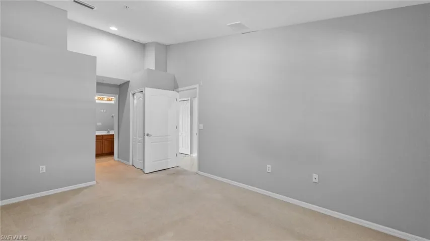 Unfurnished bedroom with light colored carpet, connected bathroom, a high ceiling, and a closet