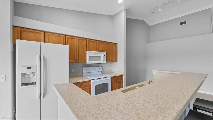 Kitchen with white appliances, ornamental molding, brown cabinets, a breakfast bar, and light stone counters