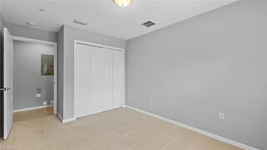 Unfurnished bedroom with light colored carpet, a closet, and electric panel
