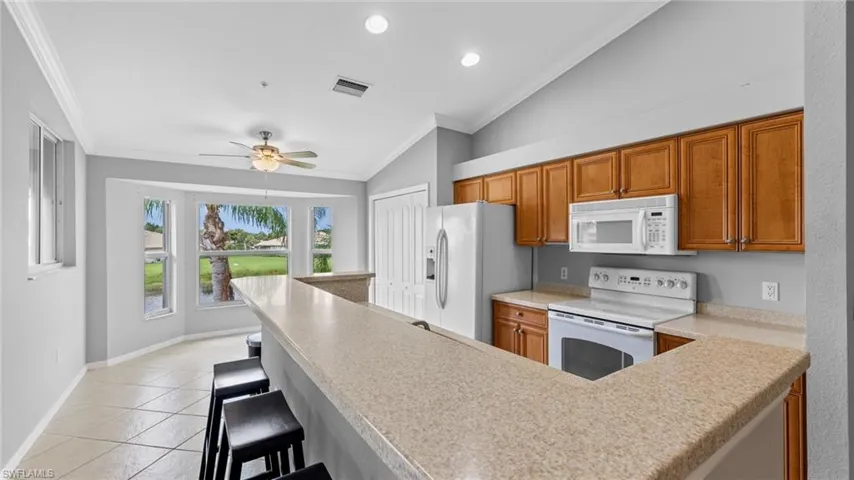 Kitchen featuring crown molding, white appliances, vaulted ceiling, a kitchen bar, and brown cabinets