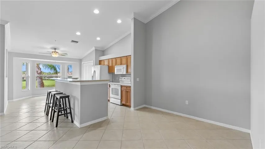Kitchen with a kitchen bar, light countertops, white appliances, lofted ceiling, and a center island with sink