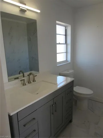 Bathroom featuring toilet, marble finish floor, vanity, and crown molding
