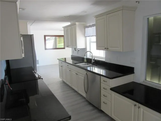 Kitchen featuring white cabinetry, a sink, dark countertops, light wood finished floors, and dishwashing machine