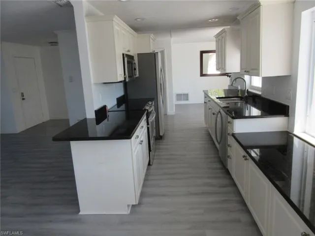 Kitchen featuring white cabinets, a sink, stainless steel appliances, and light wood-type flooring