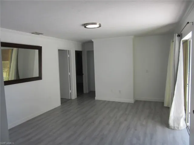 Unfurnished room featuring wood finished floors, ornamental molding, baseboards, and visible vents