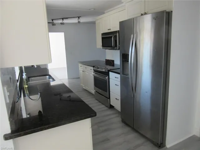 Kitchen with dark countertops, light wood-style floors, white cabinetry, and stainless steel appliances