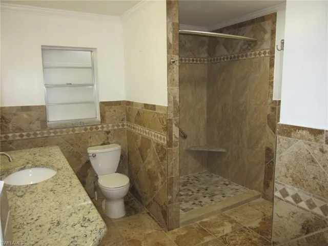 Bathroom with tile walls, toilet, tiled shower, vanity, and ornamental molding