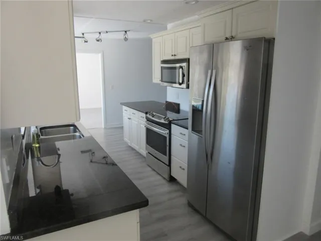 Kitchen with a sink, dark countertops, light wood-style flooring, and appliances with stainless steel finishes