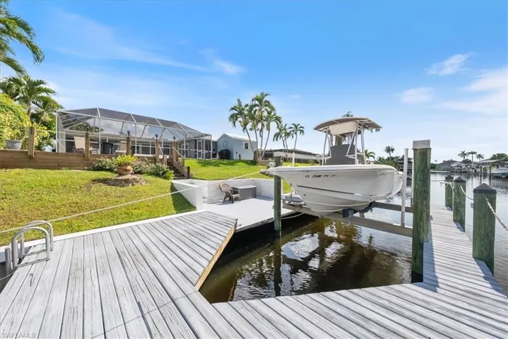 Dock area featuring boat lift, a water view, a lawn, and a lanai