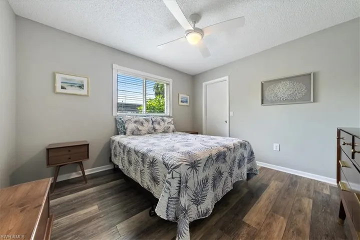 Bedroom with a textured ceiling, dark wood-style flooring, and a ceiling fan