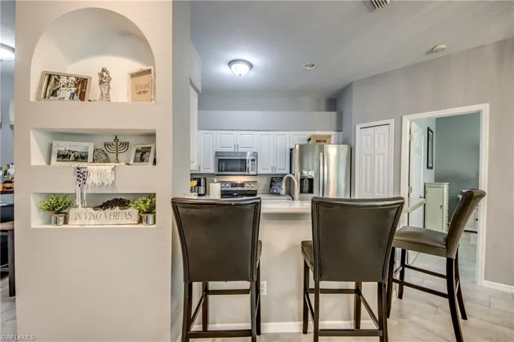 Recessed wall niches, white kitchen cabinetry, stainless steel appliances, white countertop, and tiled flooring