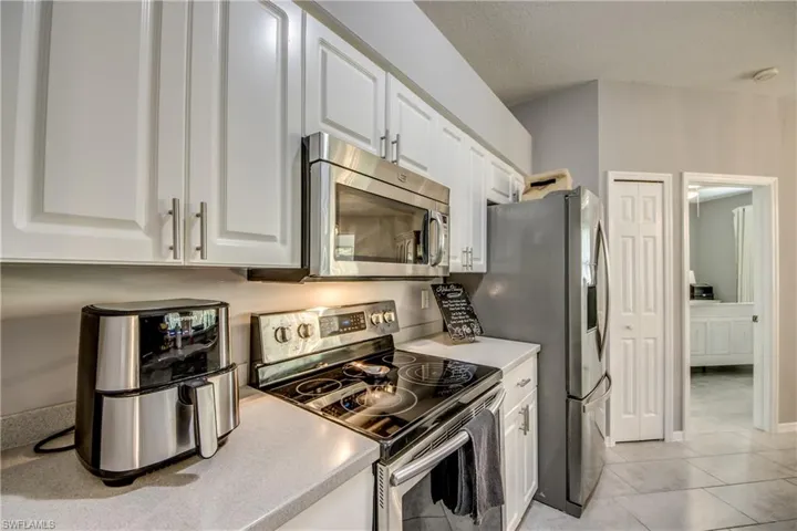 Kitchen featuring white cabinetry, stainless steel microwave, black electric range, gray refrigerator, and light gray countertops
