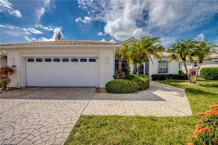 Tile roof, stucco exterior, patterned paver driveway, integrated garage, and mature landscaping