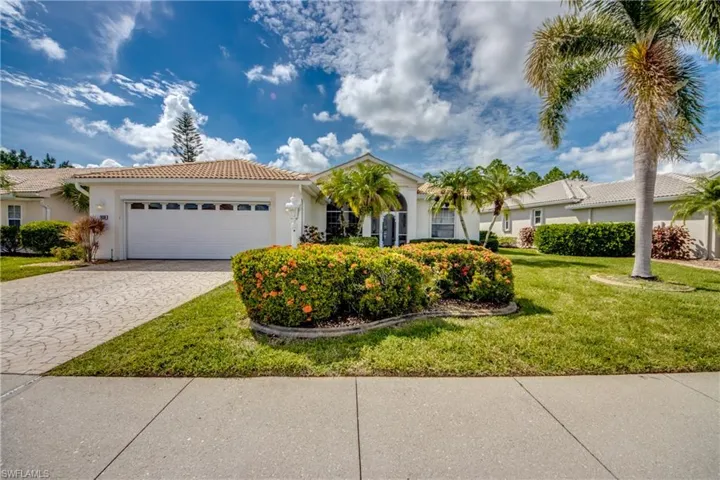 Stucco exterior with a tiled roof, patterned driveway, lush lawn, and mature landscaping