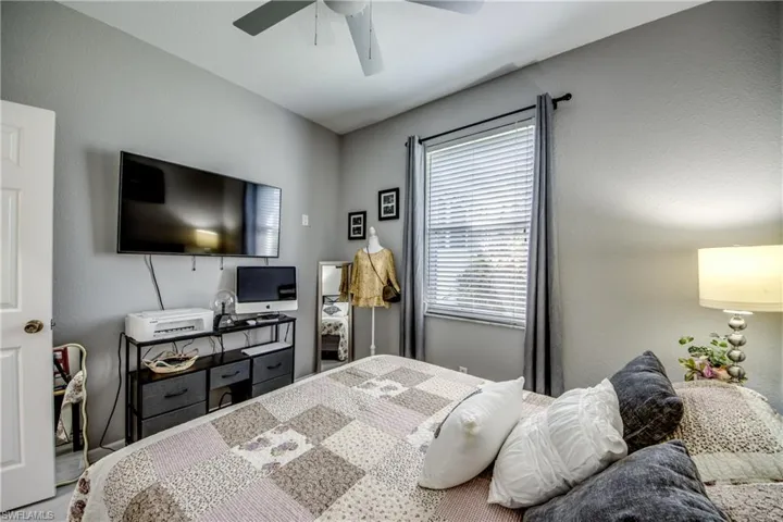 Wall-mounted television with media console, window with blinds and dark curtains, and a ceiling fan