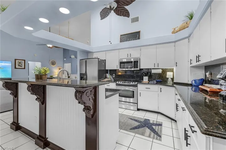 Kitchen featuring a towering ceiling, appliances with stainless steel finishes, a ceiling fan, backsplash, and light tile patterned flooring