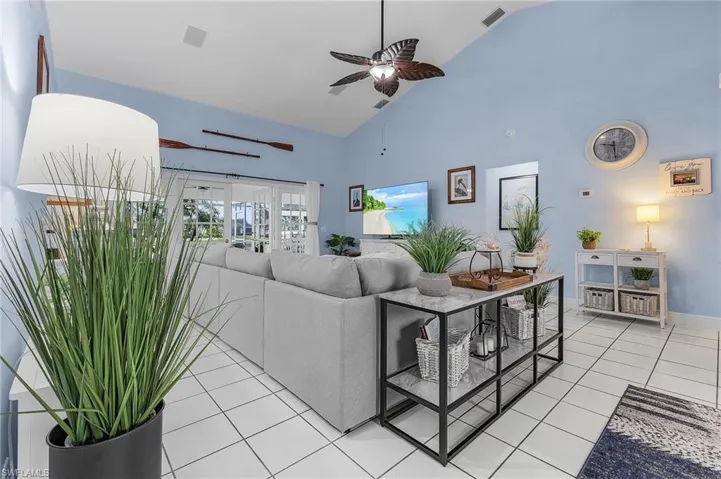 Living room with high vaulted ceiling, light tile patterned floors, a ceiling fan, and baseboards