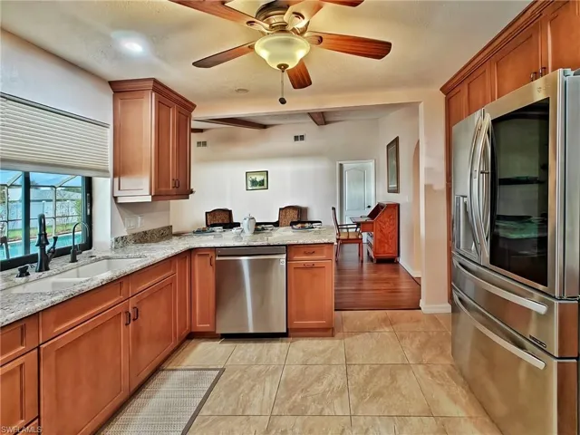 Kitchen with kitchen peninsula, appliances with stainless steel finishes, light stone countertops, ceiling fan, and sink