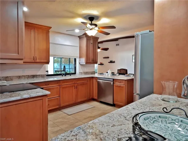 Kitchen with appliances with stainless steel finishes, light stone counters, a textured ceiling, sink, and light tile patterned flooring