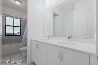 Full bathroom featuring double vanity, shower / bath combination with curtain, and light tile patterned floors
