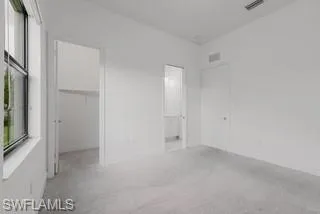 Unfurnished bedroom featuring a spacious closet, light colored carpet, and connected bathroom