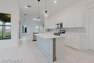 Kitchen featuring white cabinetry, light countertops, a kitchen island, pendant lighting, and backsplash