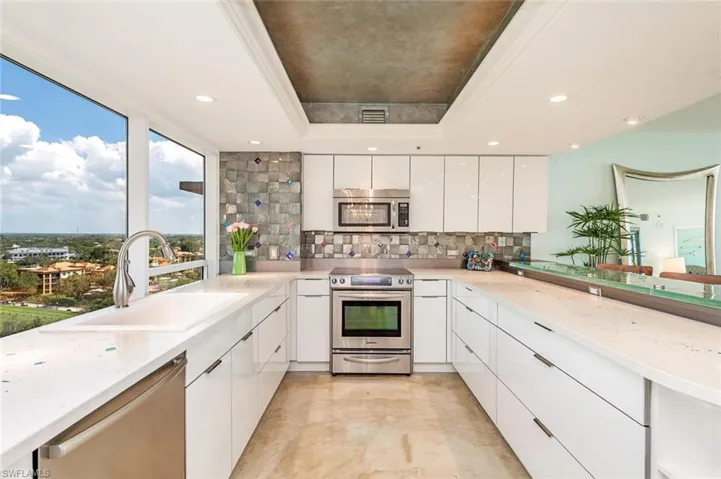 Kitchen with stainless steel appliances, white cabinets, a raised ceiling, light stone counters, and backsplash