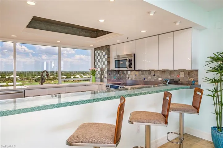 Kitchen with a tray ceiling, a kitchen breakfast bar, white cabinetry, modern cabinets, and recessed lighting