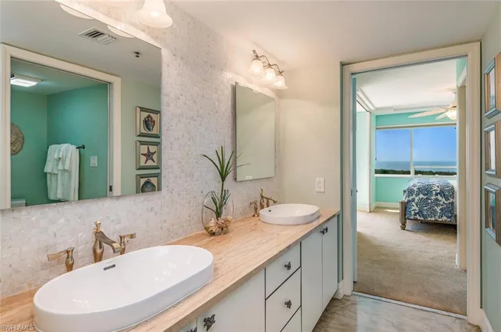 Full bath with double vanity, connected bathroom, backsplash, light colored carpet, and a water view