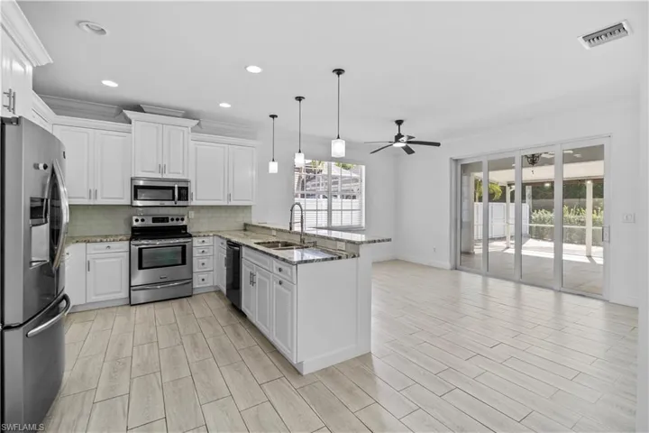Kitchen with stainless steel appliances, white cabinetry, light stone counters, a peninsula, decorative backsplash, and ornamental molding