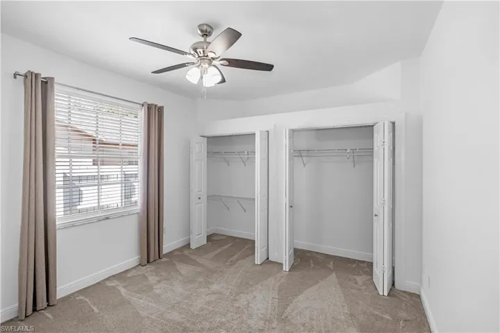 1st bedroom featuring double closets, light carpet, and a ceiling fan.