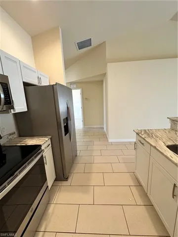 Kitchen with stove, white cabinetry, light stone countertops, light tile patterned floors, and lofted ceiling