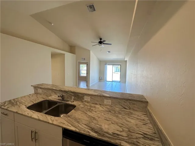 Kitchen with light stone countertops, white cabinets, a ceiling fan, stainless steel dishwasher, and vaulted ceiling