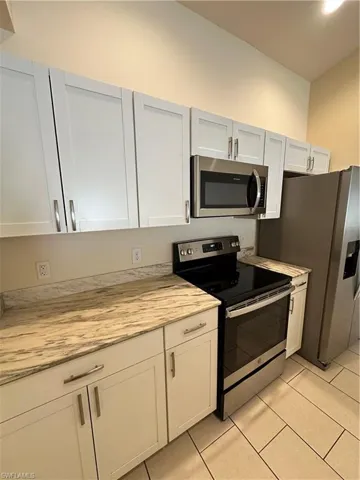 Kitchen featuring range, stainless steel microwave, light countertops, refrigerator, and white cabinets