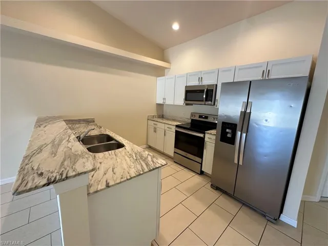 Kitchen featuring stainless steel appliances, light stone countertops, vaulted ceiling, a peninsula, and light tile patterned flooring