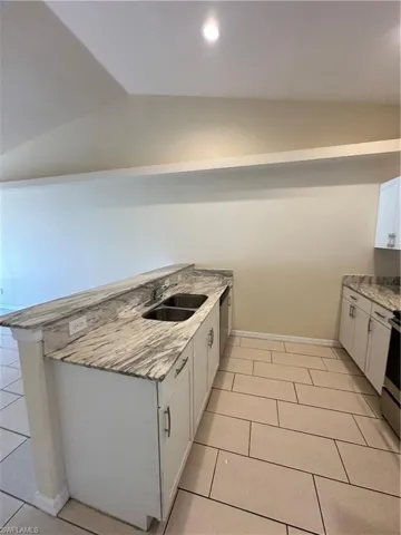 Kitchen featuring white cabinets, light tile patterned floors, range, vaulted ceiling, and recessed lighting