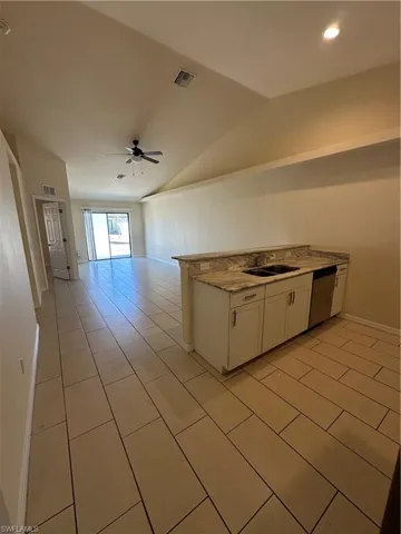 Kitchen with white cabinetry, ceiling fan, vaulted ceiling, light tile patterned flooring, and light stone countertops