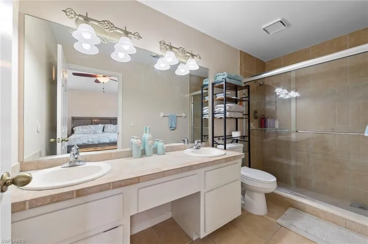 Bathroom featuring a dual vanity with integrated sinks, tile countertop, and a large mirror
