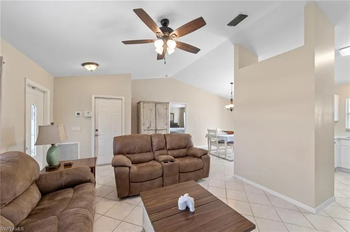 Living area featuring vaulted ceilings, a ceiling fan with light fixture, and neutral tile flooring