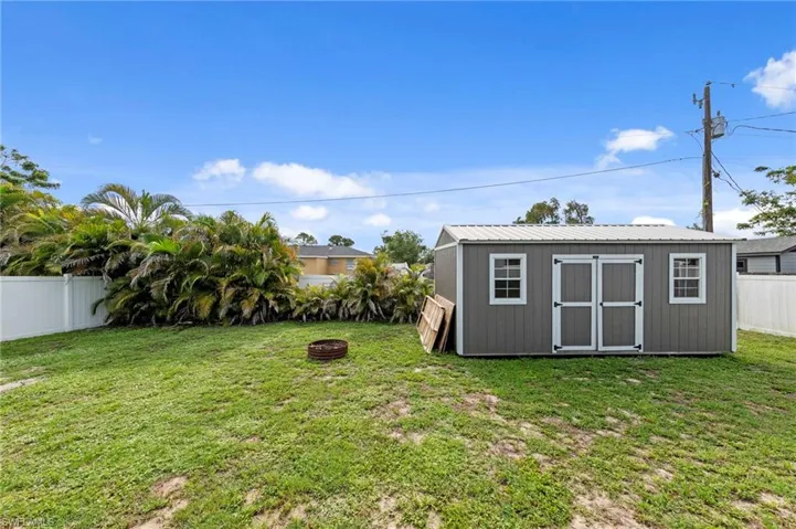 Spacious backyard featuring a gray storage shed with white trim, a metal roof, double entry doors, and two windows