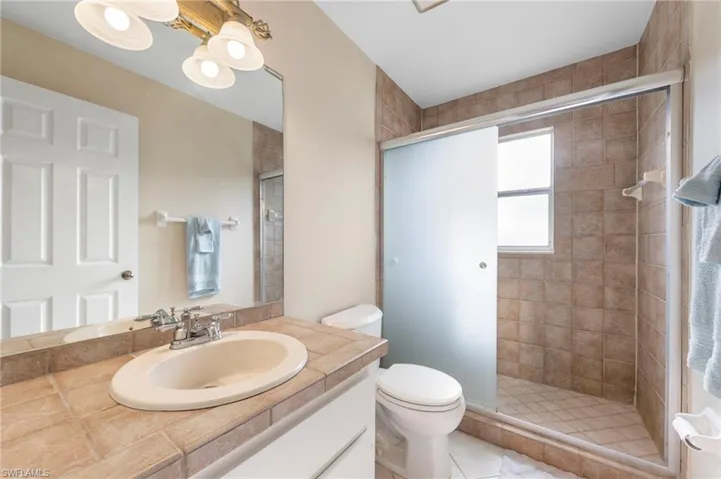 Full bathroom featuring a tiled vanity countertop, an integrated sink with a chrome faucet, a large wall mirror, and a shower enclosure with frosted glass sliding doors and a window